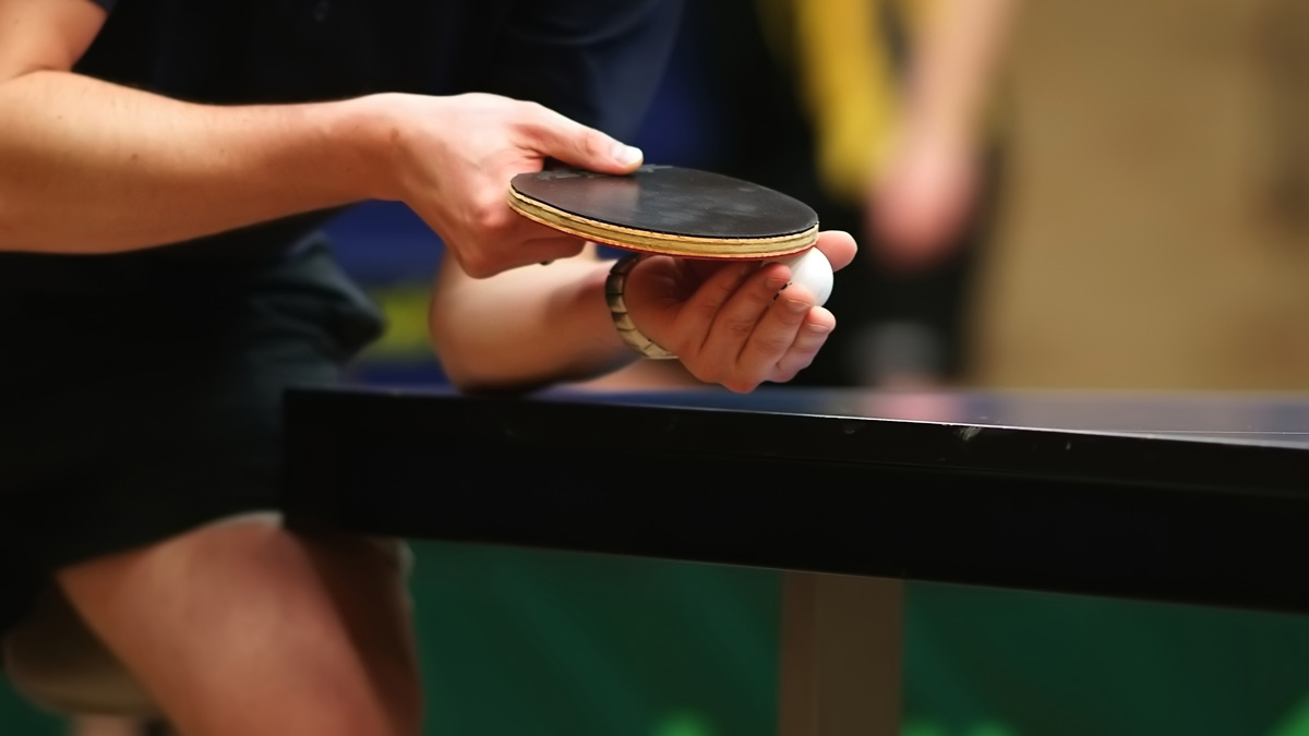 close up image of player holding ping pong ball and paddle